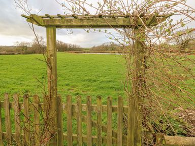 A wooden garden gate with an archway overlooking a green field with trees and a pond in the distance at Sarngwm in Narberth