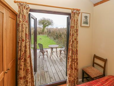 A bedroom with wooden wardrobe and chair opening to a deck with table and chairs at Sarngwm in Narberth