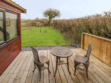 A wooden deck with a metal table and two chairs next to a grassy yard with a birdhouse and trees at Sarngwm in Narberth