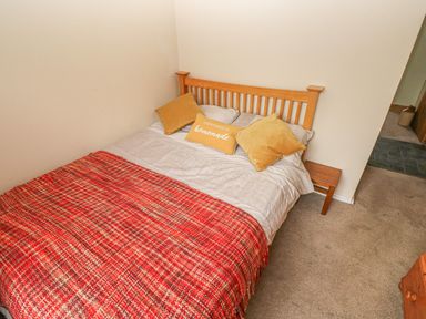 A bedroom with a bed with a wooden headboard two yellow pillows and a red blanket at Sarngwm in Narberth