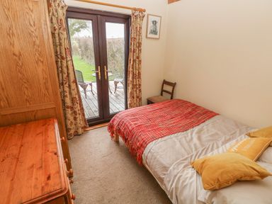 A bedroom with a single bed a wooden dresser a chair and glass doors leading outside at Sarngwm in Narberth