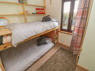 A small bedroom with wooden bunk beds and a window with pink plaid curtains at Sarngwm in Narberth