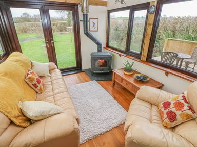 A living room with leather sofas a wood stove a coffee table and large windows showing a garden at Sarngwm in Narberth