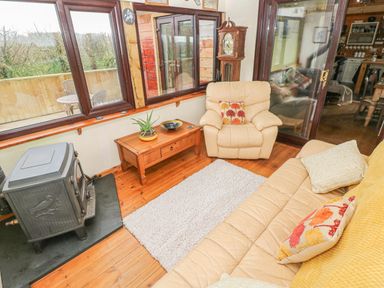 A sitting area with beige armchair and sofa a wooden coffee table a rug and a wood burner at Sarngwm in Narberth