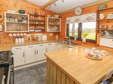 A kitchen with wooden countertops white cabinets shelves with jars dishes and cups a window with floral blinds and a sink at Sarngwm in Narberth