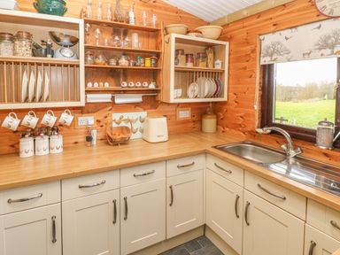 A kitchen with cream cabinets wooden countertops a stainless steel sink and wooden shelves holding jars and dishes at Sarngwm in Narberth