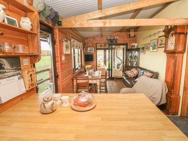 A wooden kitchen countertop with teapot and mugs looking into a dining area with a table set for four and a living room with sofa and grandfather clock at Sarngwm in Narberth