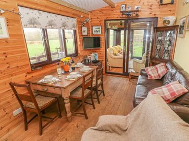 A dining area with a wooden table set for four and chairs a brown leather sofa with cushions wooden floors and walls with windows and glass doors at Sarngwm in Narberth
