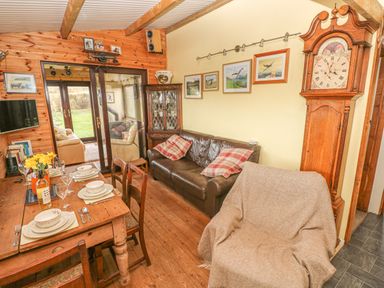 A dining area with a wooden table set for four people a leather sofa with pillows a wooden cabinet and a grandfather clock at Sarngwm in Narberth