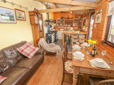 A kitchen dining area with a wooden table set for four with dishes and wine next to a leather sofa and a tall grandfather clock at Sarngwm in Narberth