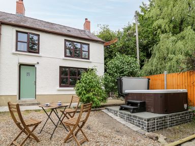 A backyard with wooden chairs and table with cups and a hot tub near a white house with green door and brown windows at Fisherman's Cottage in Llandysul