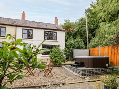 A backyard with a wooden table and chairs a hot tub and plants at Fisherman's Cottage in Llandysul