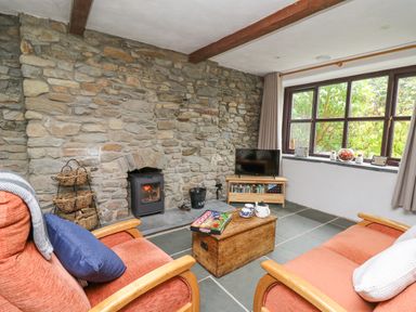 A living room with stone wall fireplace two armchairs wooden chest coffee table and window at Fisherman's Cottage in Llandysul