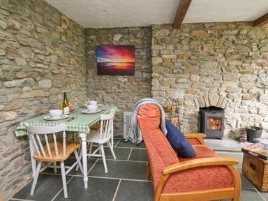 A dining area with a table set for four and a red sofa facing a wood stove in a room with stone walls at Fisherman's Cottage in Llandysul