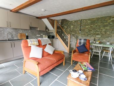 A kitchen and sitting area with orange chairs, stone wall, wooden beams, and a dining table at Fisherman's Cottage in Llandysul