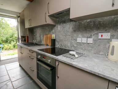 A kitchen with cabinets a sink an oven a stove and an open door leading outside at Fisherman's Cottage in Llandysul