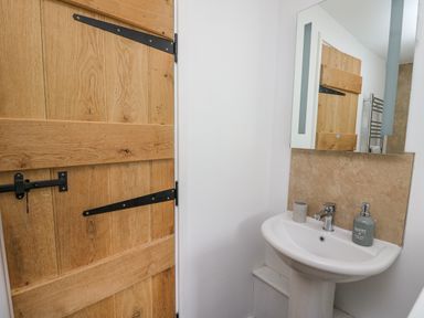 A small bathroom with a wooden door pedestal sink a mirror and soap dispenser at Fisherman's Cottage in Llandysul