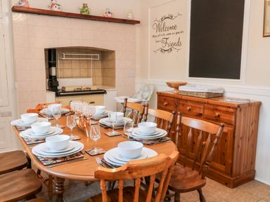 A dining room with a wooden table set for six, wooden chairs, a sideboard, and a tiled fireplace at The Vale in Ashwater
