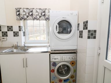 A laundry area with a stacked white dryer and a washing machine with flower stickers next to a stainless steel sink and window at The Vale in Ashwater