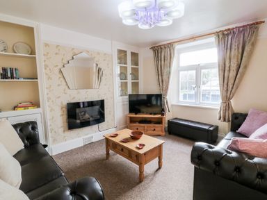 A living room with two black sofas a wooden coffee table a mounted television and a window with curtains at The Vale in Ashwater