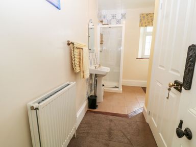 A bathroom with a shower enclosure a pedestal sink a towel rack with towels a radiator and a window at The Vale in Ashwater
