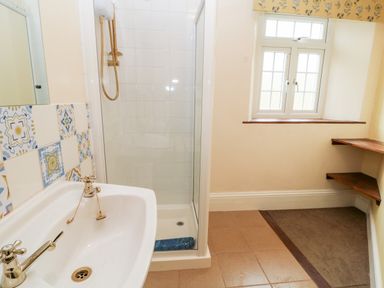 A bathroom with a sink shower and a window with shelves at The Vale in Ashwater