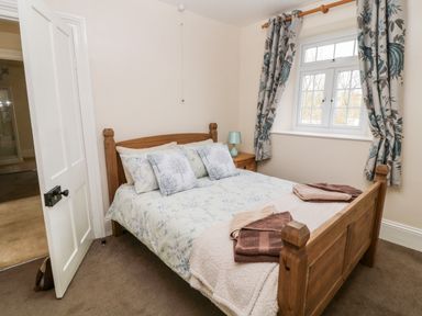 A bedroom with a wooden bed a window with curtains a nightstand and a lamp at The Vale in Ashwater