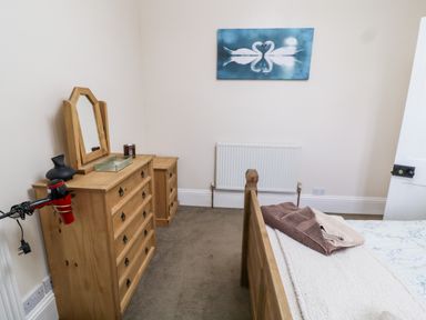 A bedroom with a wooden dresser and mirror a hair dryer on the dresser towels on a bed a swan picture on the wall at The Vale in Ashwater