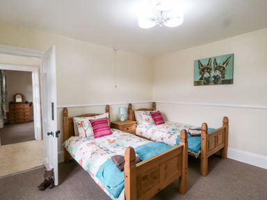A bedroom with two single wooden beds a nightstand with a lamp and a painting of two donkeys on the wall at The Vale in Ashwater