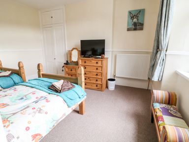 A bedroom with twin wooden beds a wooden dresser with a TV and a small mirror and a colorful bench at The Vale in Ashwater