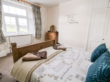 A bedroom with a wooden bed and chest of drawers next to a window at The Vale in Ashwater