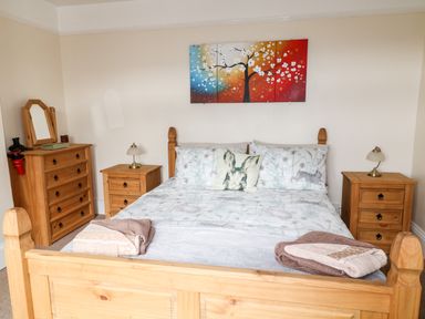 A bedroom with a wooden double bed flanked by two wooden bedside tables with lamps and a wooden dresser with a mirror at The Vale in Ashwater