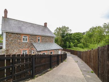 A stone house with white framed windows beside a paved driveway and wooden fences at The Vale in Ashwater