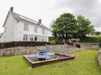 A backyard with a white house a wooden sandbox and trees at The Vale in Ashwater