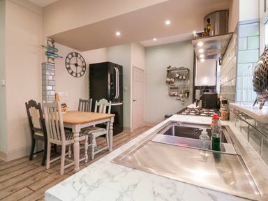 A kitchen with a wooden dining table and four chairs a black refrigerator a gas stove a stainless steel sink and utensils on the wall at Saxon Lodge Cottage in Felixstowe Suffolk