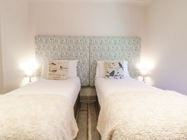 A bedroom with two single beds with bird patterned headboards and lamps on either side at Saxon Lodge Cottage in Felixstowe Suffolk