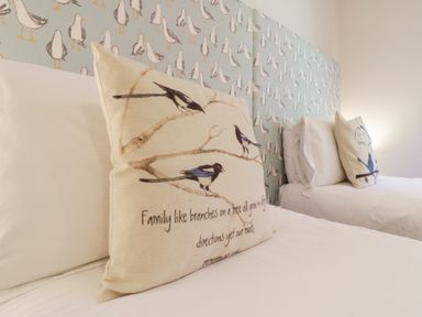 Two beds with white linens and decorative pillows with bird designs by a patterned headboard at Saxon Lodge Cottage in Felixstowe Suffolk