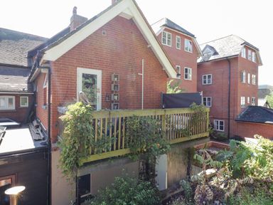 The exterior of a brick building with a wooden balcony and some plants at Saxon Lodge Cottage in Felixstowe Suffolk