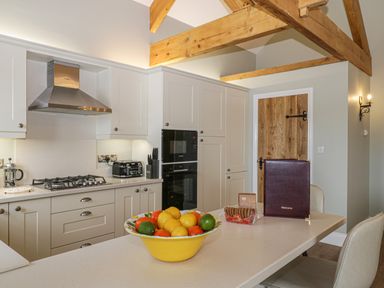 A kitchen with white cabinets wooden ceiling beams a wooden door a yellow fruit bowl on the counter and a welcome book at Shipswheel Cottage at Broadings Farm Whitby