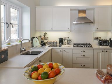 A kitchen with white cabinets a stainless steel sink a fruit bowl on the counter and a stove with a range hood at Shipswheel Cottage at Broadings Farm Whitby