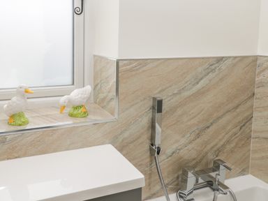 A bathroom corner with a bathtub tap shower handheld and ceramic duck decorations on the window ledge at Shipswheel Cottage at Broadings Farm in Whitby
