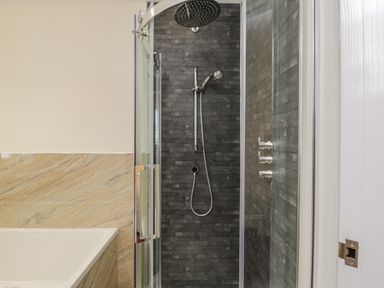 A bathroom shower with glass door and black tiled walls next to a bathtub with beige marble panel at Shipswheel Cottage at Broadings Farm Whitby