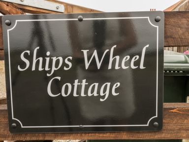 A black and white sign reading Ships Wheel Cottage on a wooden fence at Shipswheel Cottage at Broadings Farm Whitby