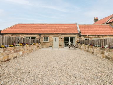 A stone house with a red tiled roof and a gravel courtyard with flowerbeds and a picnic table at Shipswheel Cottage at Broadings Farm in Whitby
