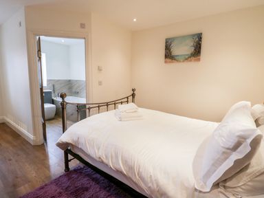 A bedroom with a metal bed frame with white bedding and folded towels with an open door leading to a bathroom at Shipswheel Cottage at Broadings Farm in Whitby