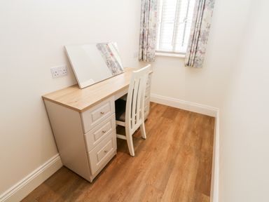 A small room with a wooden desk and white chair under a window with floral curtains at Shipswheel Cottage at Broadings Farm in Whitby