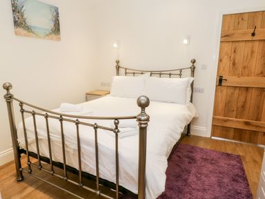 A bedroom with a metal bed frame white bedding wooden door and a purple rug on wooden floor at Shipswheel Cottage at Broadings Farm in Whitby