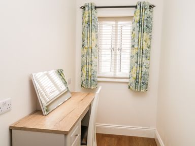 A small room with a wooden desk and a mirror on top next to a window with floral curtains at Shipswheel Cottage at Broadings Farm Whitby