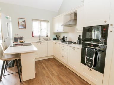A kitchen with white cabinets a gas stove oven microwave chairs and wooden floor at Shipswheel Cottage at Broadings Farm Whitby