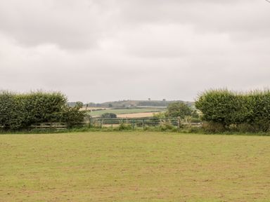 A field with grass a gate and hedges with hills and trees in the background at Shipswheel Cottage at Broadings Farm in Whitby